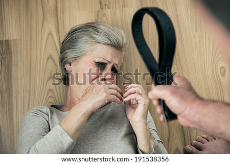 Woman victim of domestic violence and abuse. Mature woman with black eye scared of a man with a belt.