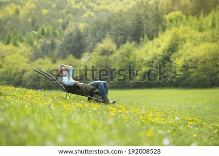 Young male farmer is relaxing in wheelbarrow on the green meadow