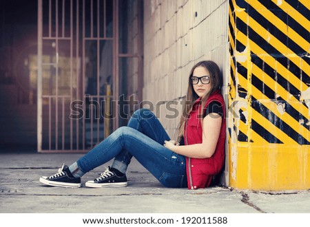 Sad teenage hipster girl sitting by the black and yellow striped warning wall