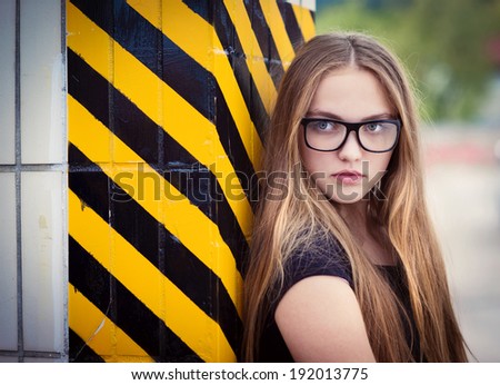 Portrait of sad teenage hipster girl standing by the black and yellow striped warning wall