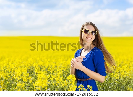 Happy young girl in blue dres nad sunglasses enjoying free time in yellow colza field