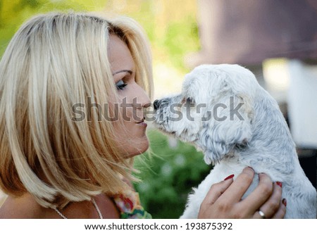 Beautiful young blonde woman is hugging and playing with her cute puppy outdoor