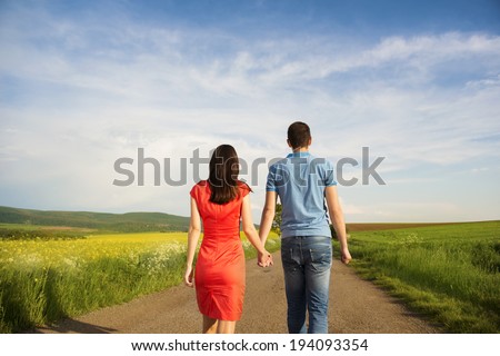 Happy young couple in love walking and holding hands on countryside road next to the colza field