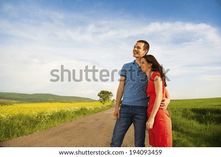 Happy young couple in love hugging on countryside road next to the colza field