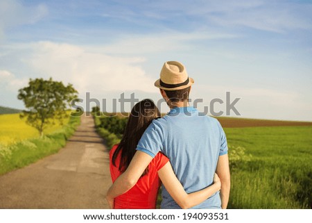 Happy young couple in love hugging on countryside road next to the colza field