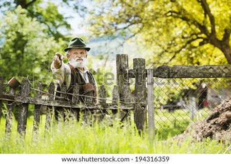 Old farmer with beard and hat standing by the lath fence with empty tins on top