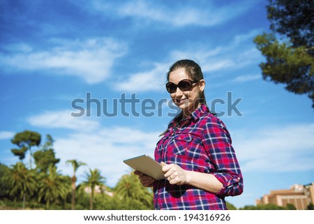 Pretty young female tourist using digital tablet, portrait with blue sky