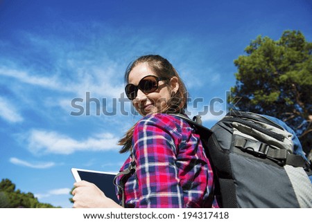Pretty young female tourist with backpack using digital tablet, portrait with blue sky