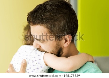 Indoor portrait of young father hugging his little daughter