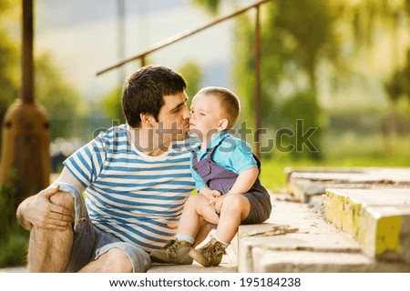 Outdoor portrait of young father kissing his little son