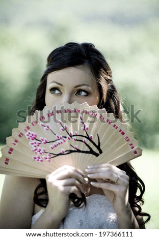 Bride in white wedding dress and summer fan posing at the meadow