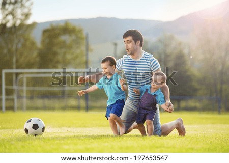 Young father with his little sons playing football on football pitch