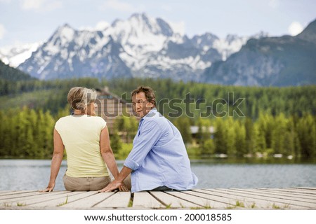Senior couple sitting on pier above the mountain lake with mountains in background