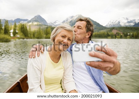 Senior couple on boat with mountains in background taking selfie