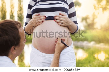 Man is writing a name on pregnant woman\'s belly in nature