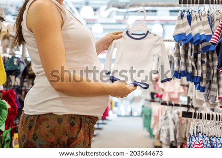 Young pregnant woman choosing baby clothes at baby shop store