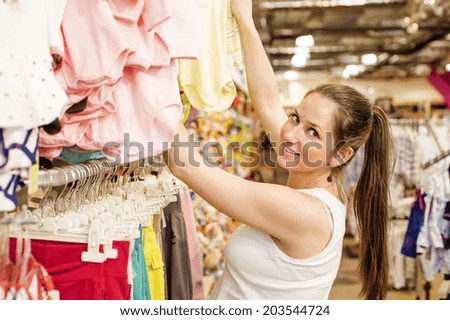 Young pregnant woman choosing baby clothes at baby shop store