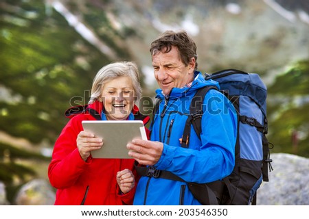 Senior hiking couple using travel app or map on tablet during the hike.