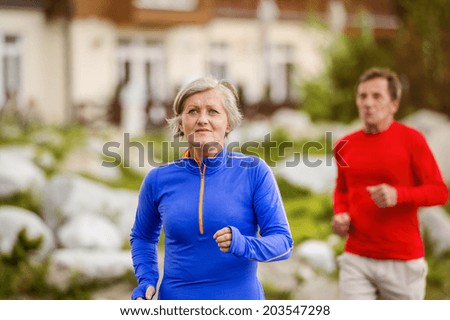 Senior couple jogging round the tarn in beautiful mountains, hills and hotel in background