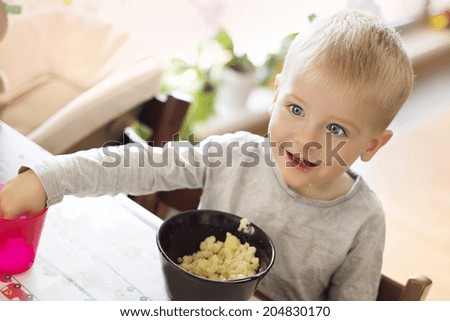 Cute little blonde boy eating pasta from black bowl