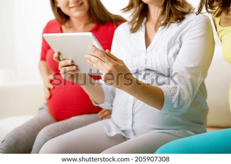 Three unrecognizable pregnant women sitting on sofa, chatting and using digital tablet