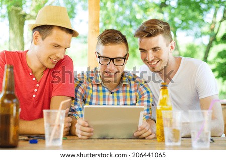 Three happy friends drinking and having fun with tablet in pub garden