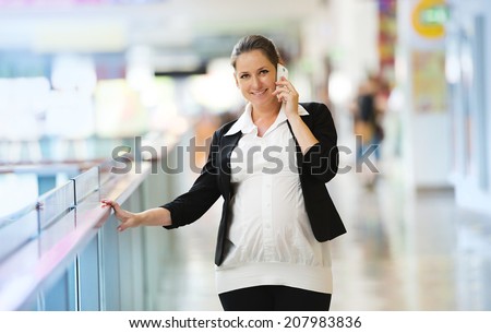 Busy pregnant woman talking on the phone in shopping mall