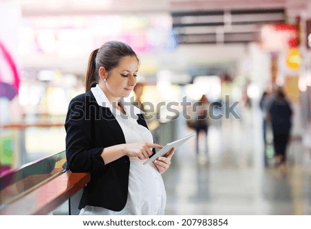 Busy pregnant woman using tablet in shopping mall