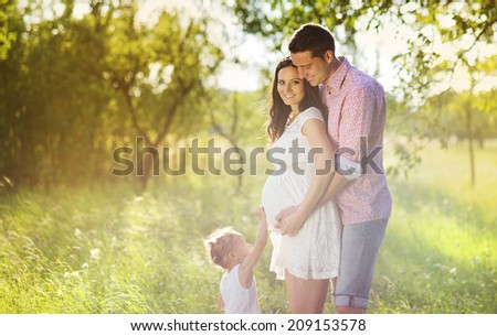 Happy pregnant couple with daughter touching belly in summer nature