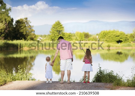 Happy young father fishing on the lake with his little daughters