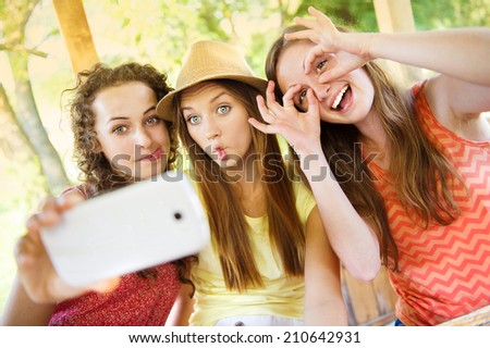 Three beautiful girls drinking and taking selfie with smartphone in pub garden