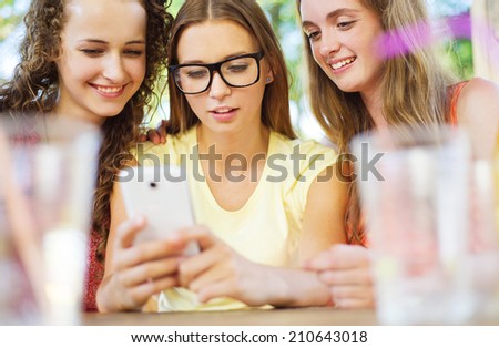 Three beautiful girls drinking and having fun with smartphone in pub garden