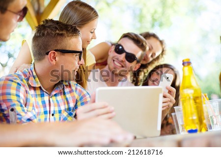 Group of happy friends drinking and having fun with tablet in pub garden