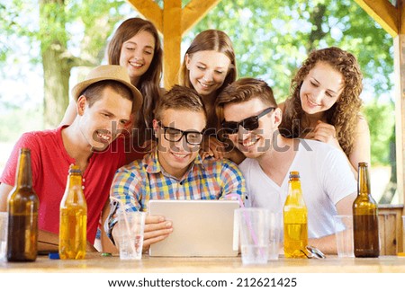 Group of happy friends drinking and having fun with tablet in pub garden