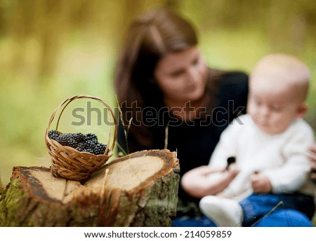 Happy young mother spending time with her baby son in forest picking and eating berries. Focus on the basket with berries