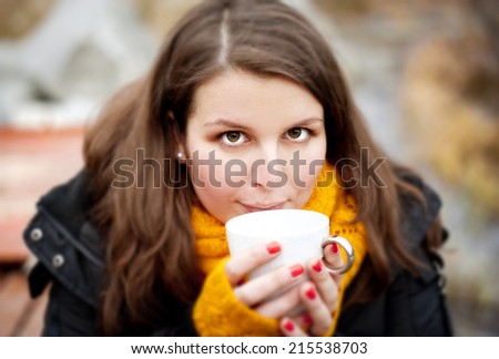 Outdoor portrait of beautiful woman in winter holding a cup with hot drink