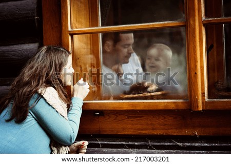 Happy family is enjoying time together. mother is outside looking through the window to her husband and liitle son