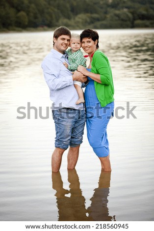 Happy young family spending summer time together by the lake on the sandy beach