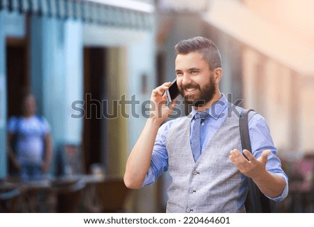 Handsome hipster modern businessman with beard walking in town and calling on mobile phone
