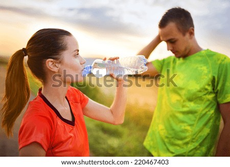 Cross-country trail running couple having water break at sunset
