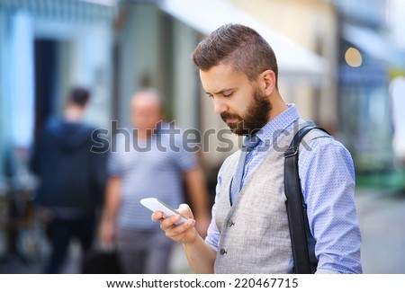 Handsome hipster modern businessman with beard walking in town with mobile phone