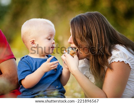 Cute little boy is feeding mother with muffin cake in nature