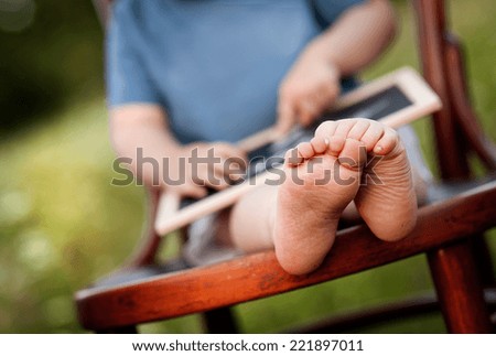 Close up of little boy drawing on little blackboard sitting on chair in meadow