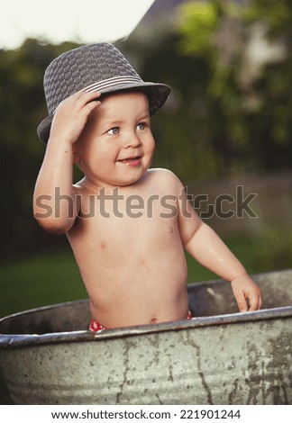 Cute funny little boy in hat bathing in galvanized tub outdoor in green garden