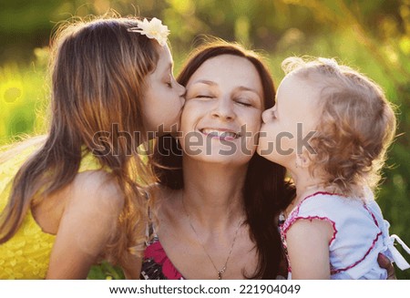 Portrait of young happy mother with her little daughters in sunny meadow