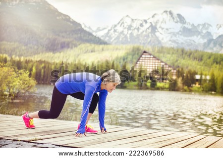 Senior woman is getting ready jogging round the tarn in beautiful mountains, hills and hotel in background