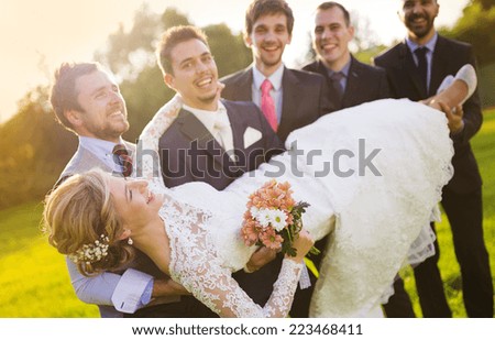 Outdoor portrait of young groom with his friends holding beautiful bride