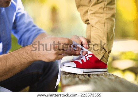 Father is helping his son to tie his shoes in summer nature