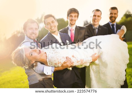 Outdoor portrait of young groom with his friends holding beautiful bride