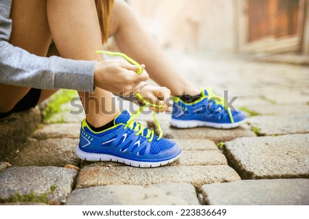 Female athlete tying sport shoes laces for running on tiled pavment in city center. Runner getting ready for training.